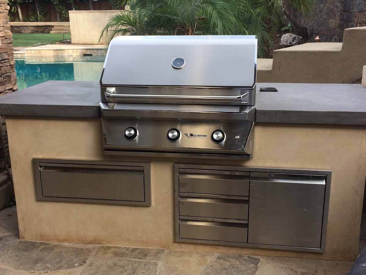 Built-in grill island with concrete countertop beside a pool