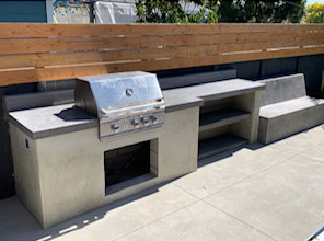 Modern concrete-topped BBQ island with a floating concrete bench and wood privacy screen