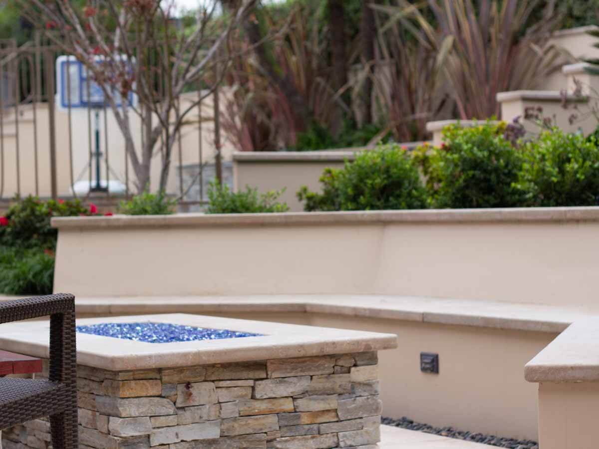Stacked stone fire pit with a travertine cap in a terraced backyard