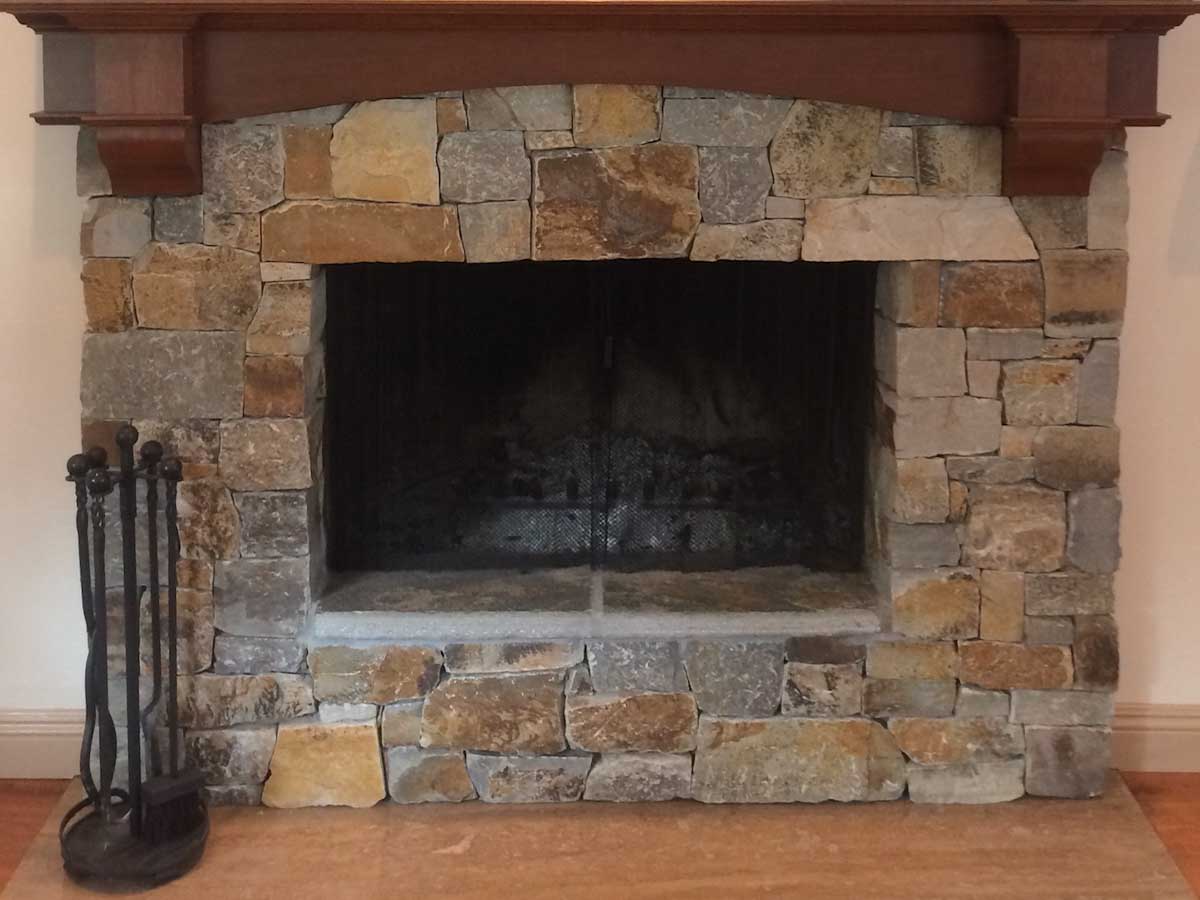 Indoor natural stone fireplace surround with a wood mantel