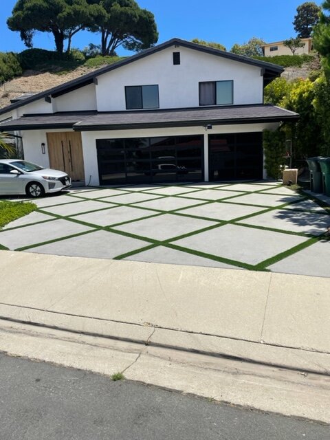 Modern concrete driveway with large panels and turf grid joints in front of a black and white home
