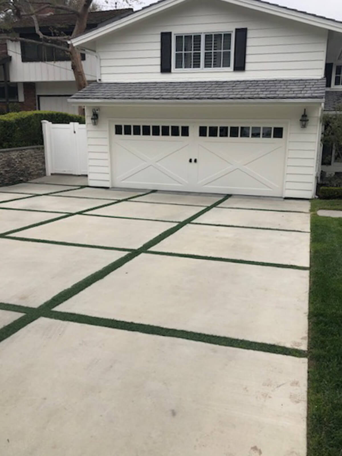 White concrete driveway panels separated by artificial turf strips in front of a black garage door