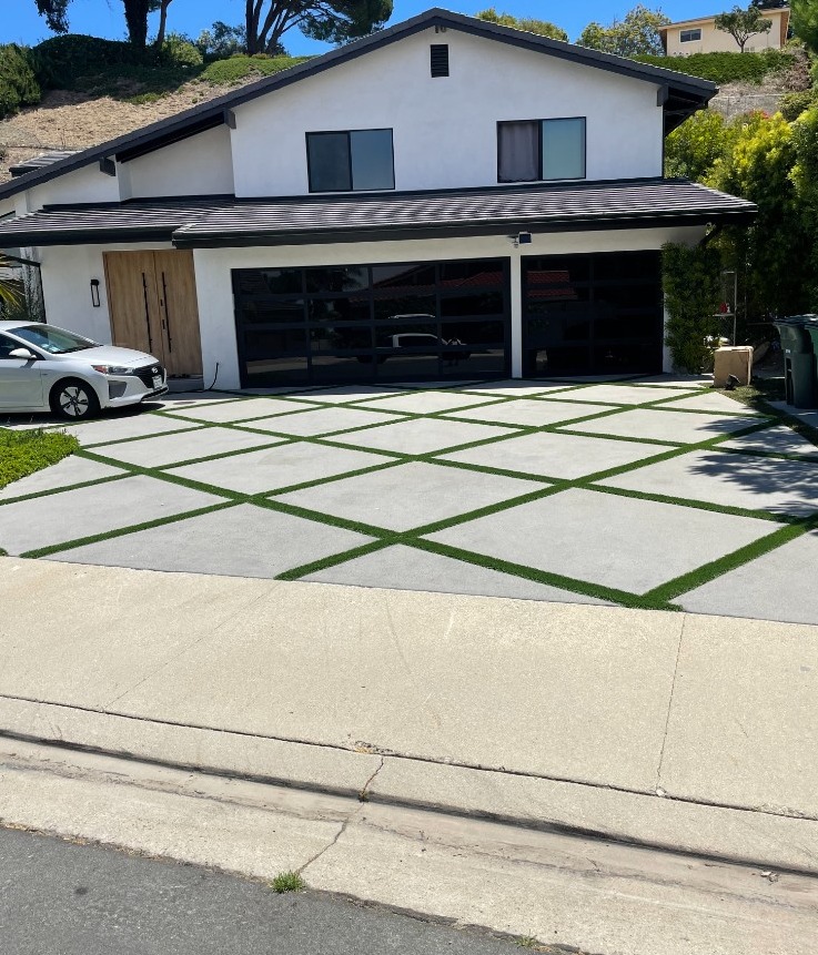 Diamond-pattern concrete driveway with turf ribbon joints leading to black glass garage doors