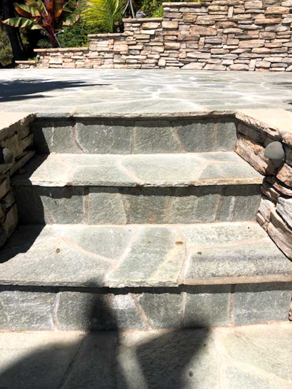 Broad steps with dark slate flagstone treads set into a flagstone patio
