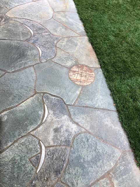 Dolphins playing with a ball, inlaid in cut stone along a slate walkway beside a lawn