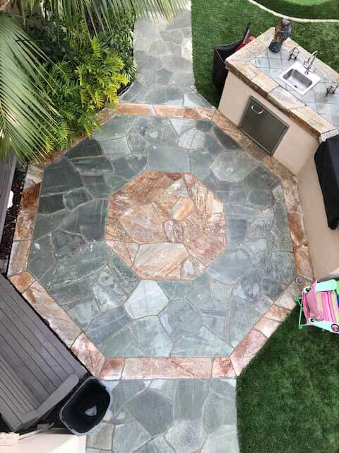 Octagon medallion of rose and green slate set into a stone patio beside an outdoor kitchen