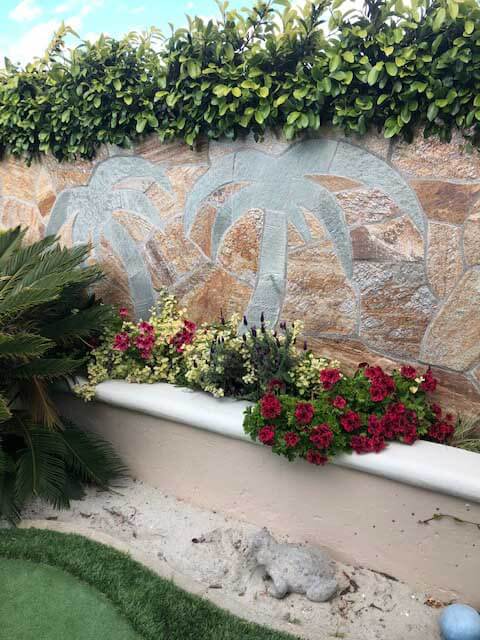 Palm trees and a sun inlaid in green slate on a stone veneer garden wall above a planter