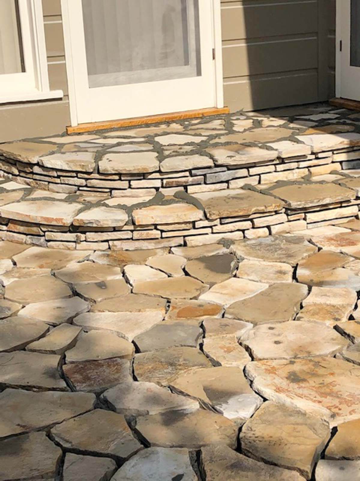 Curved Lompoc stone steps rising from a flagstone patio to a doorway