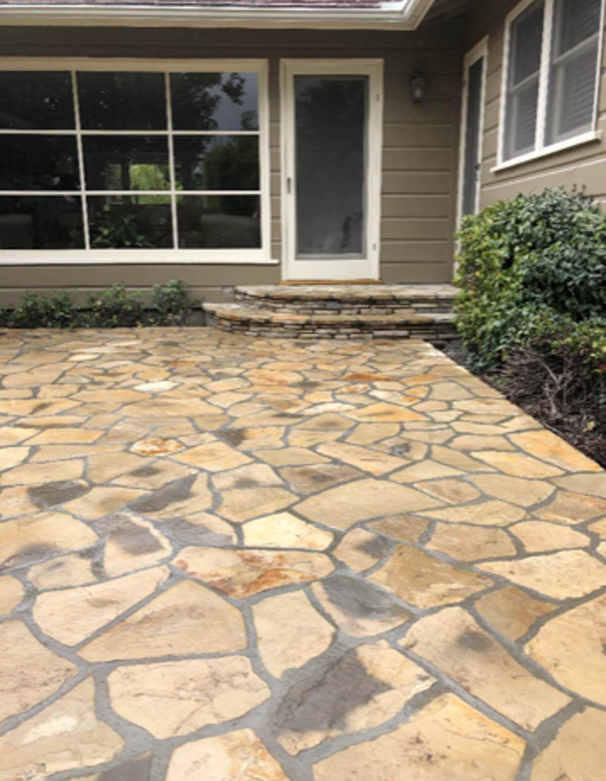 Lompoc stone patio in warm buff tones fronting a home with large windows