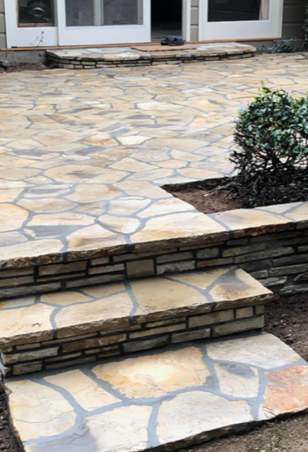 Lompoc stone patio with steps and a low stone seat wall beside a planter