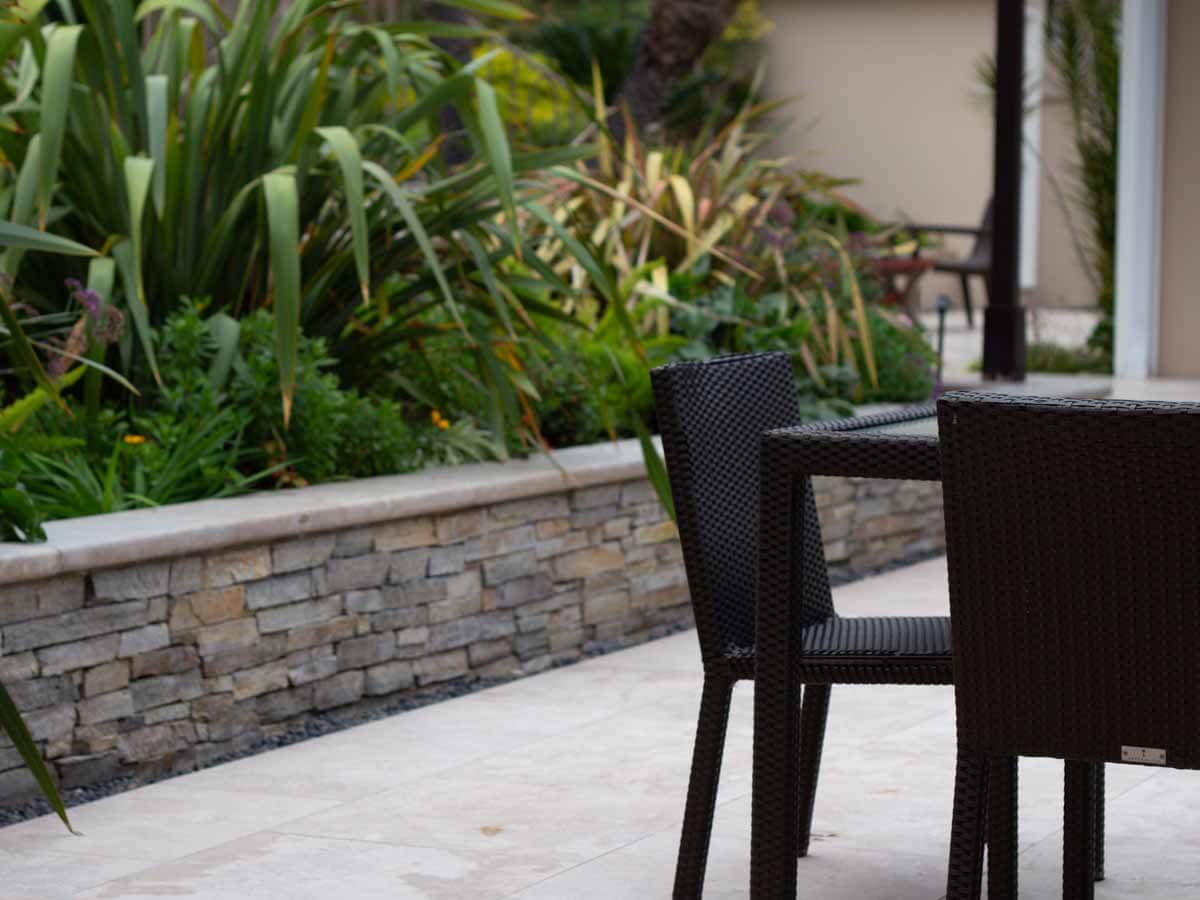 Stacked stone planter wall with a stone cap along a travertine patio dining area