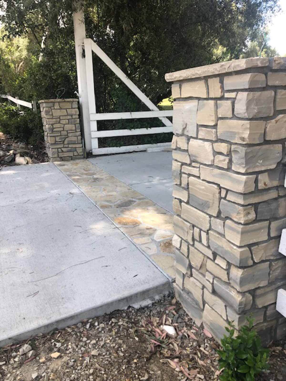 Stone veneer entry columns flanking a driveway with a white rail fence