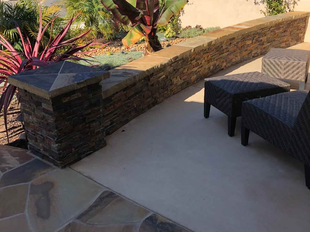 Low stacked stone seat wall with a flagstone cap beside a concrete patio
