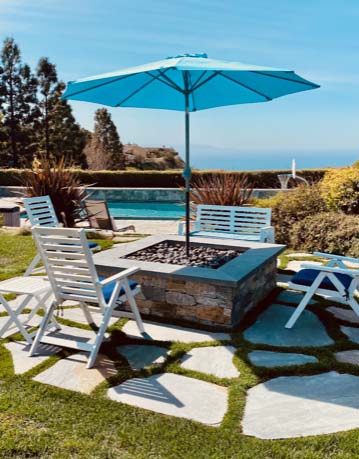 Fire pit and lounge chairs on a stone and turf patio overlooking the water