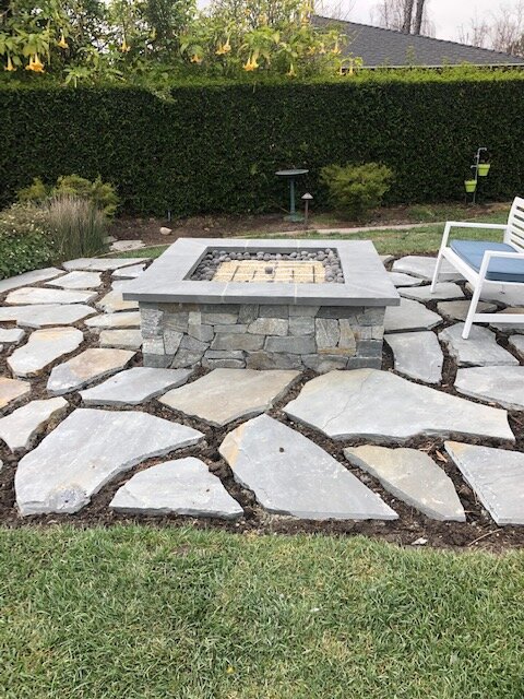Flagstone patio around a square stone fire pit set into a lawn