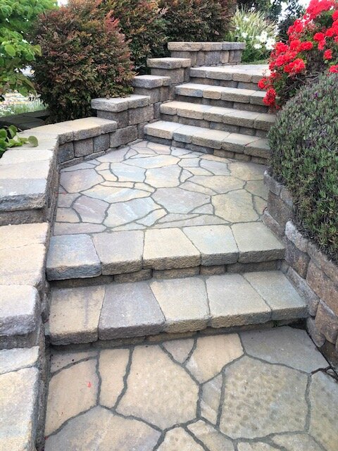 Flagstone steps and walkway climbing a slope between paver-block garden walls and roses