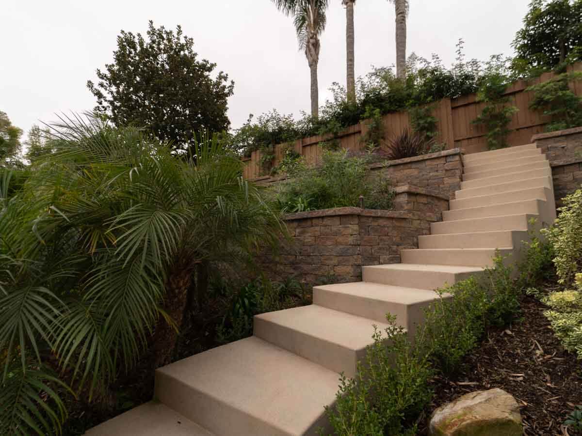Long colored concrete staircase climbing a hillside beside a stone-faced retaining wall