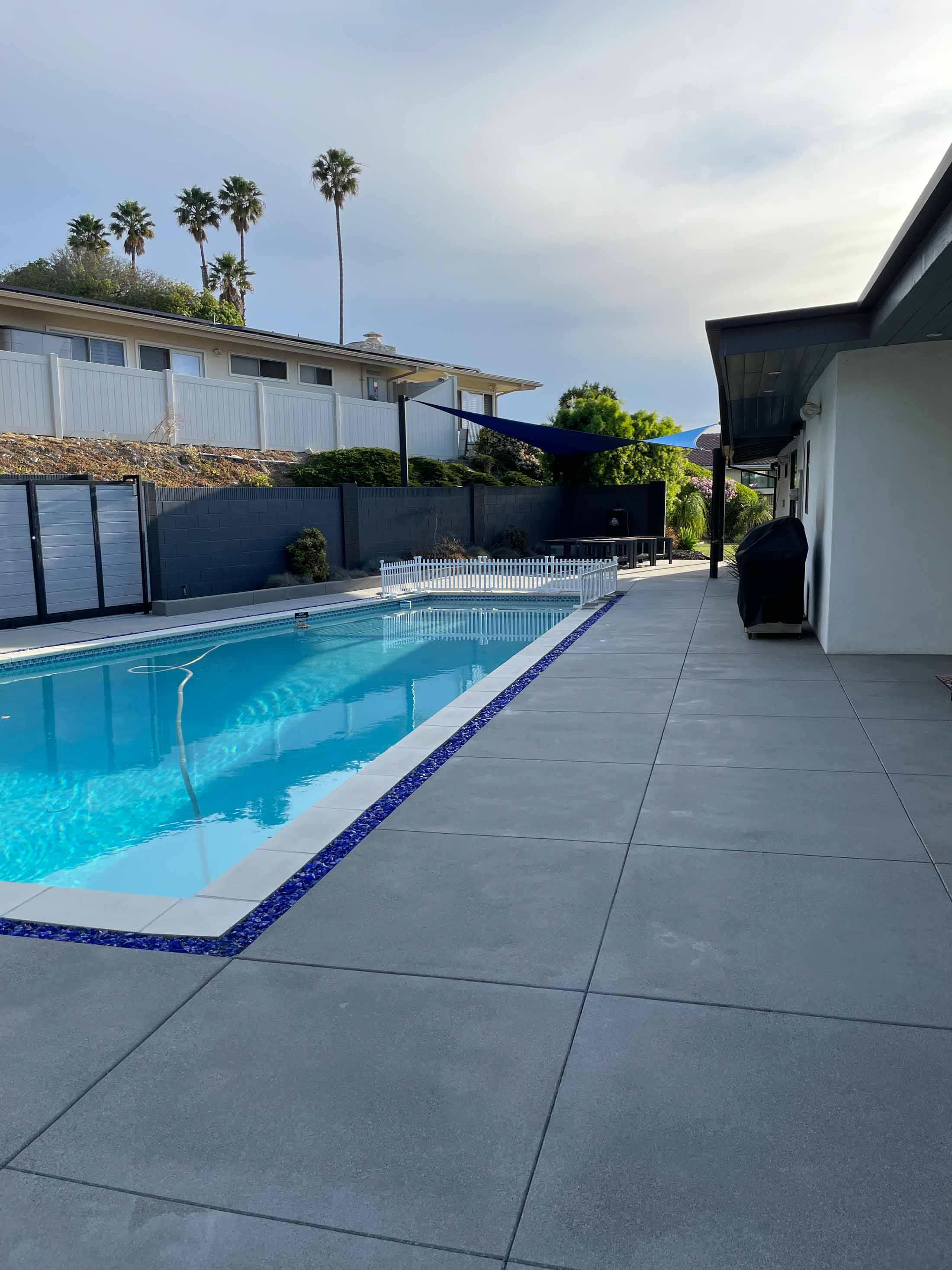 New concrete deck running the length of a pool toward a black slat privacy screen
