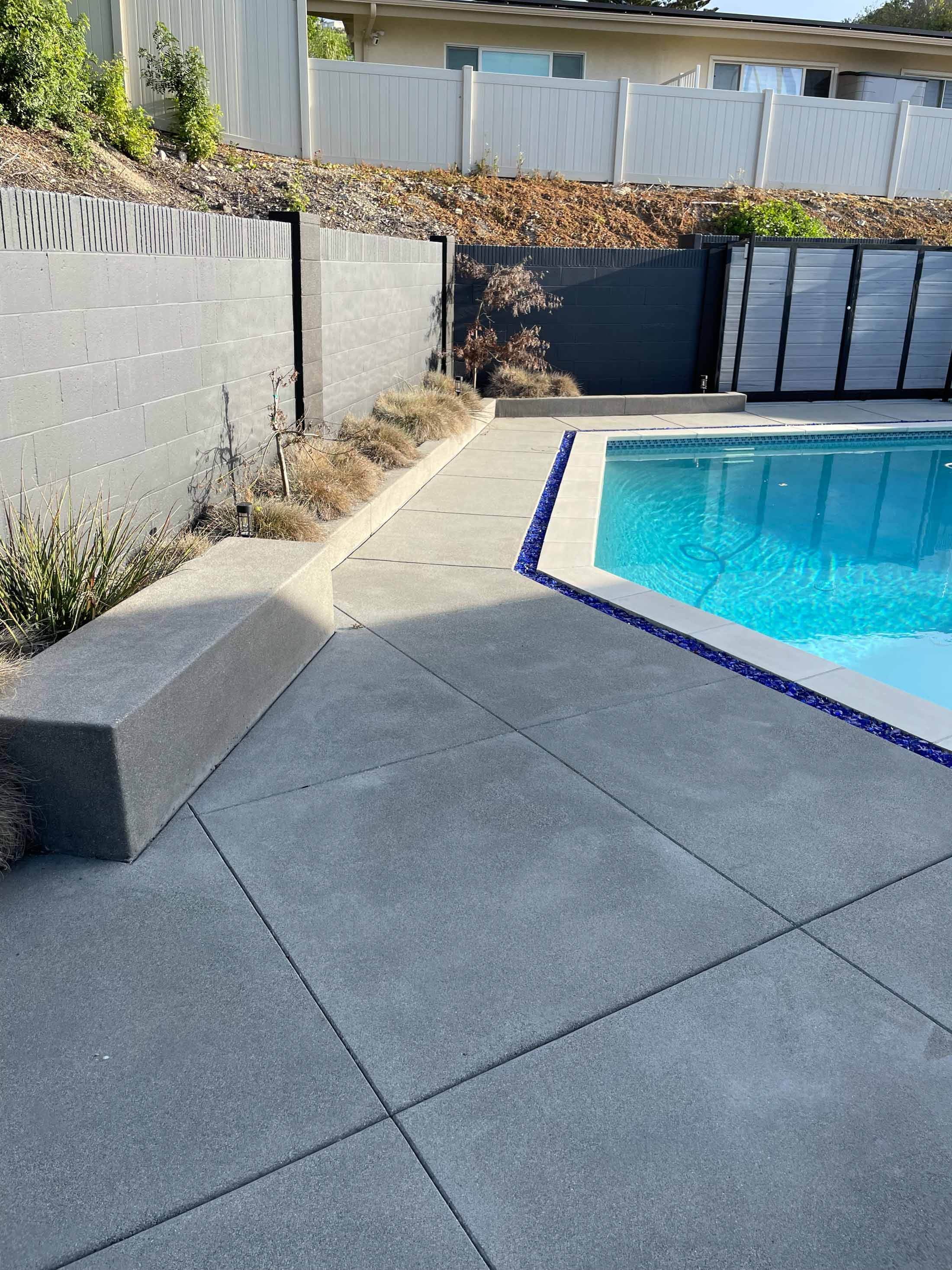 Freshly poured gray concrete pool deck with a poured-in-place tapered bench