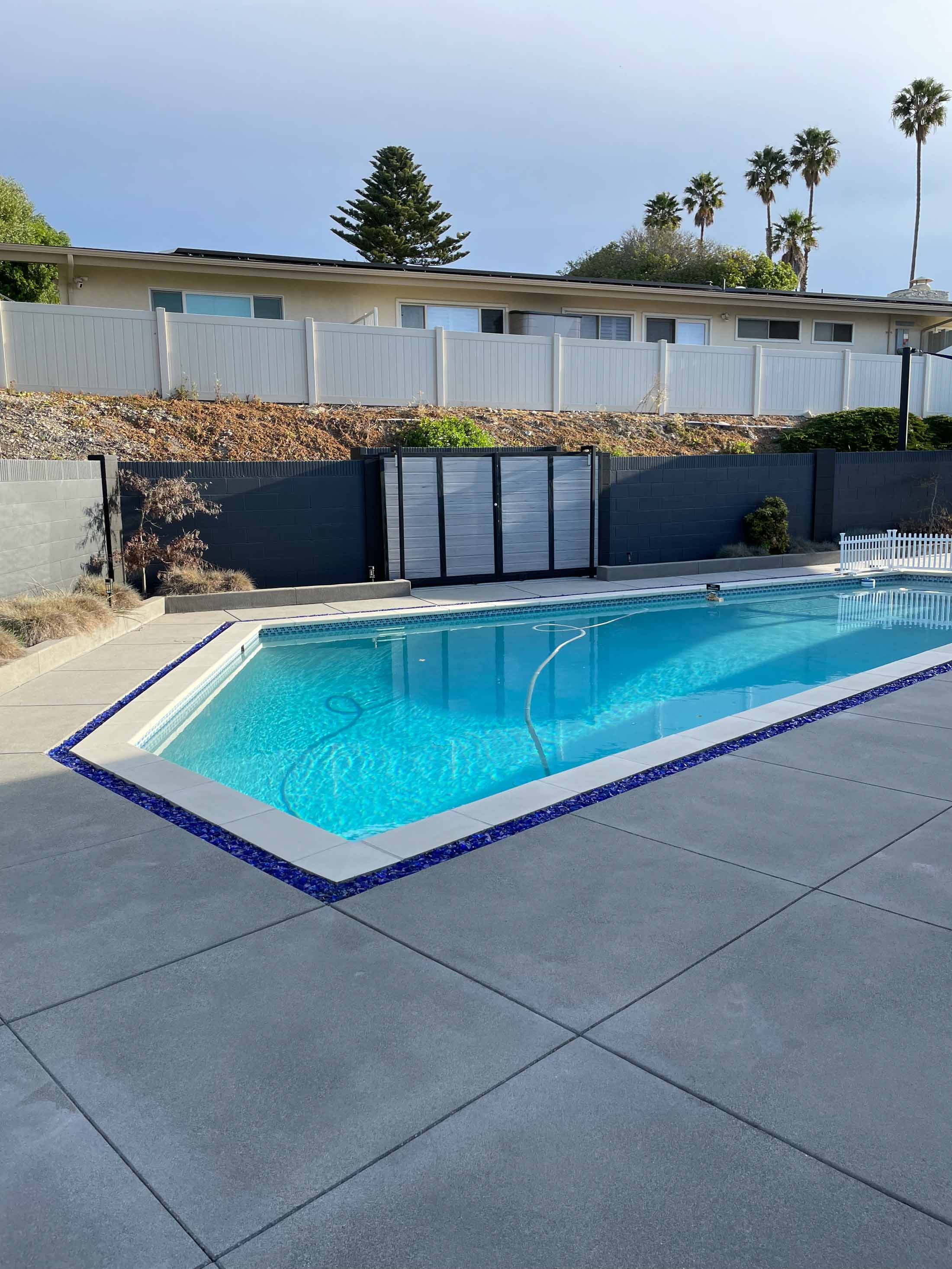 Pool with a blue glass-capped drainage trough and white coping surrounded by a new gray concrete deck