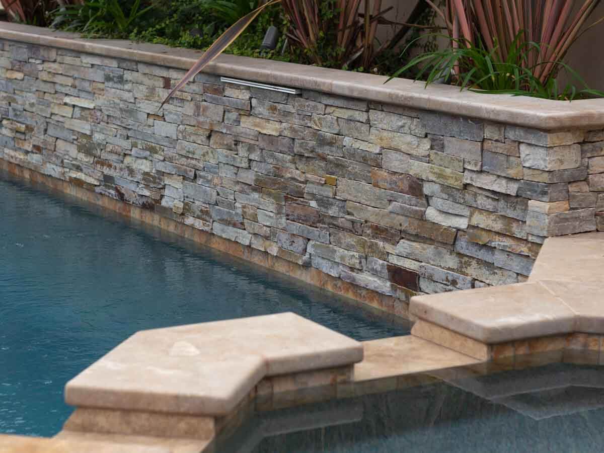 Close-up of a stacked stone raised wall and travertine coping meeting the water