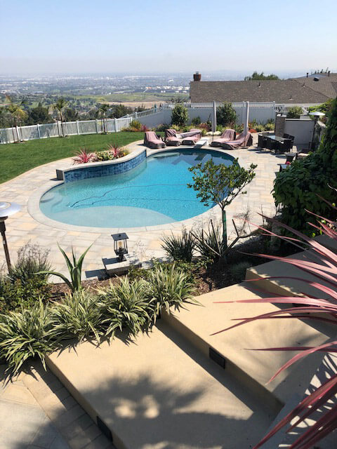 Elevated view of a freeform pool with a tan deck and planted beds overlooking the city