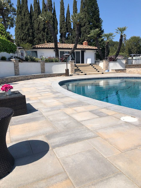 Blended gray and tan paver pool deck curving around a pool toward a Spanish-style pool house