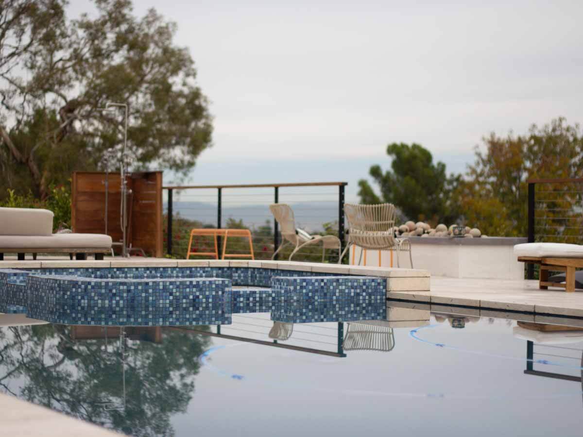 Raised spa faced in blue glass tile with an overflow edge, coastline in the distance