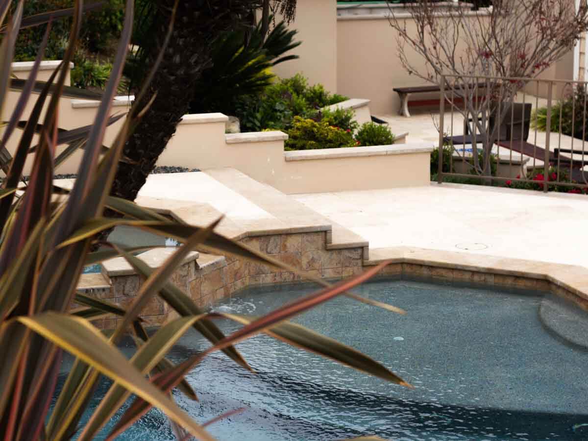 Travertine steps climbing terraced planters beside a pool