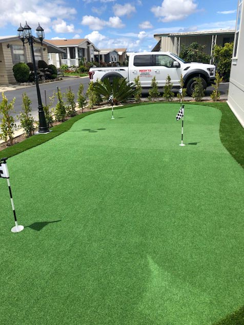 Putting green with three flags running alongside paver paving and new hedge plantings