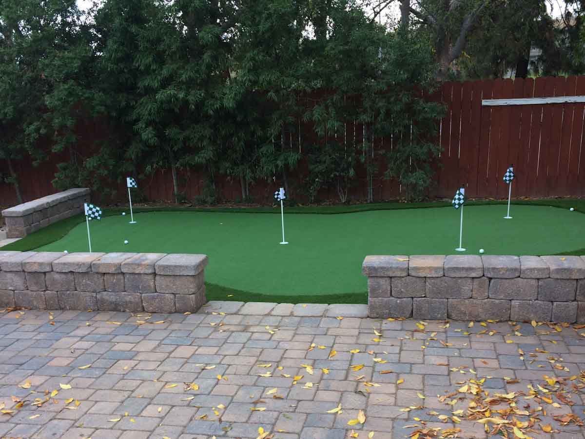 Corner putting green with five flags framed by two low block seat walls and a tumbled paver patio