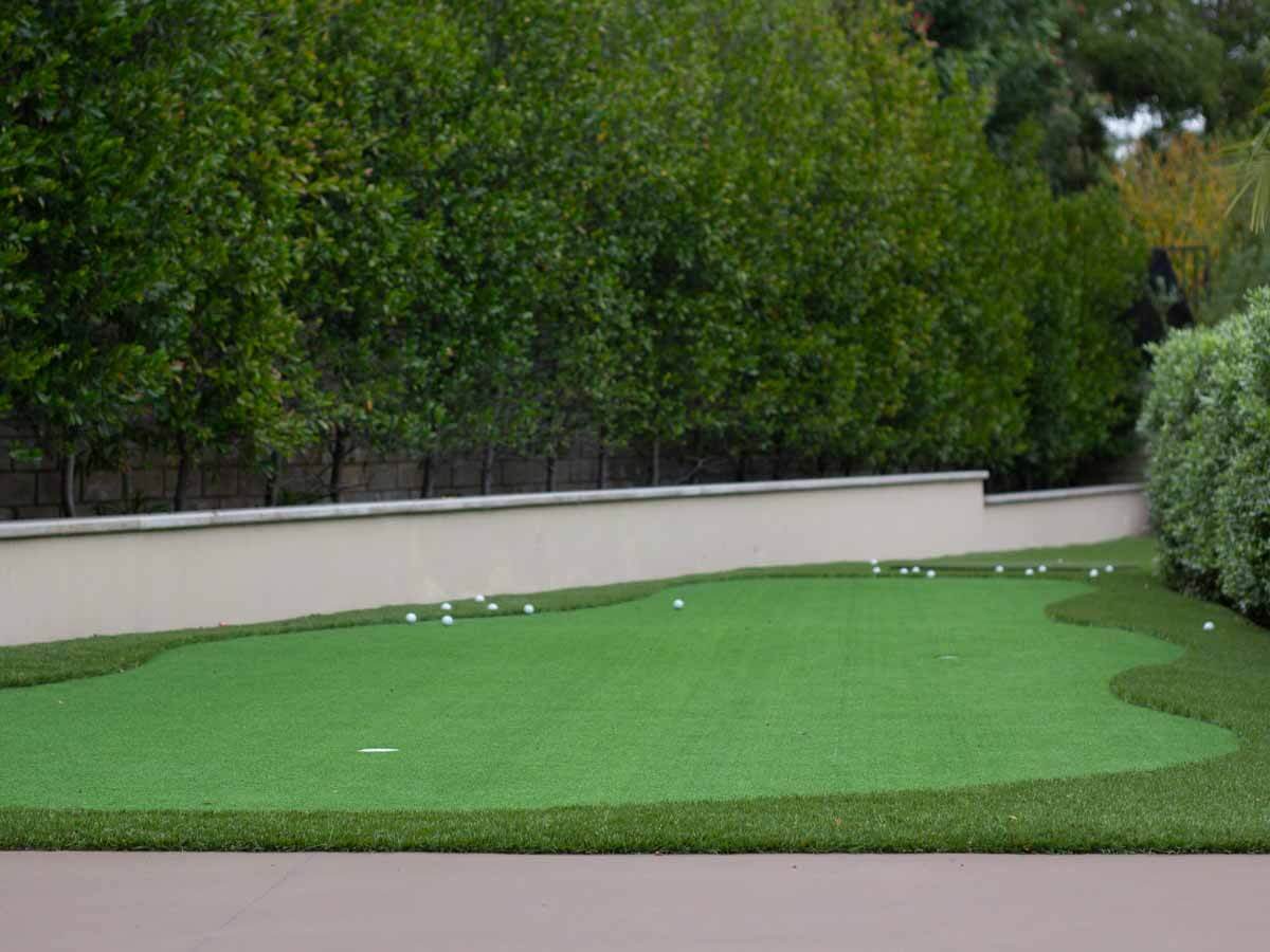 Long putting green with contoured fringe running along a white stucco retaining wall