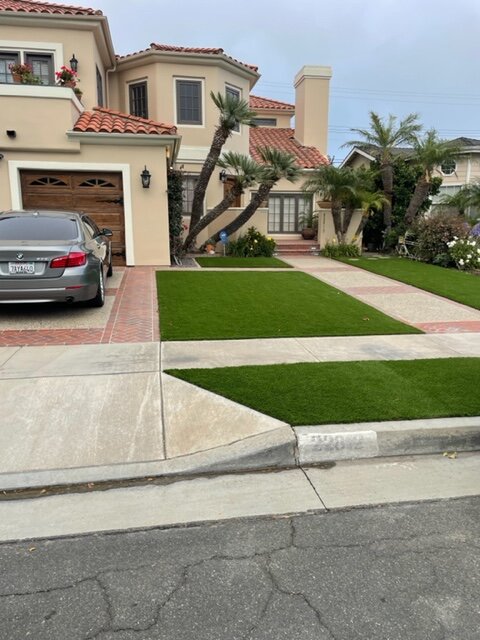 Concrete driveway panels separated by artificial turf ribbons in front of a Spanish-style home