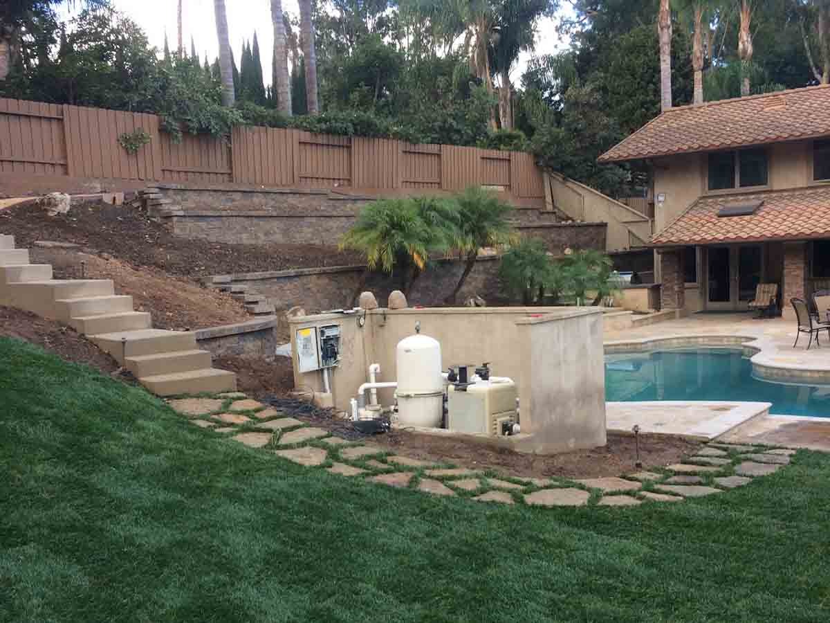 Terraced stacked-stone retaining walls climbing a hillside behind a pool, with flagstone steppers