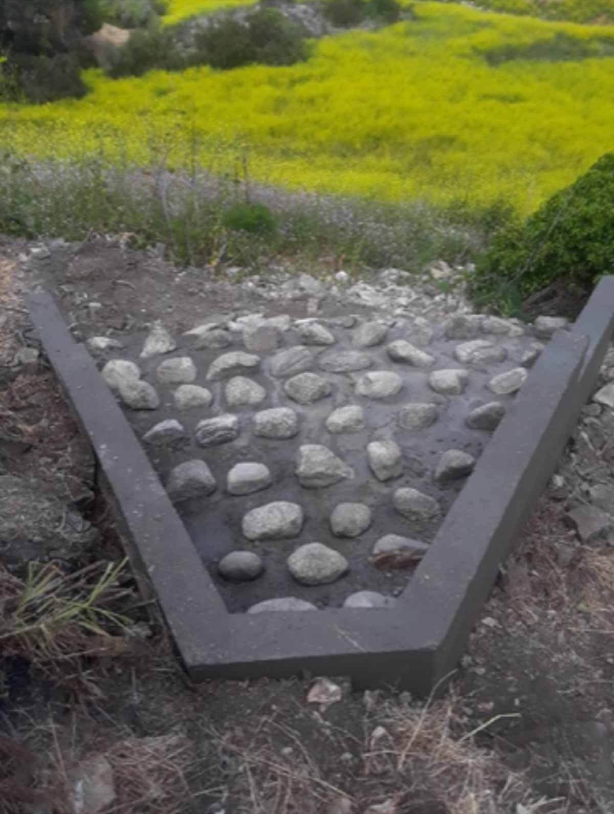 Rock-lined drainage channel running down a hillside of spring wildflowers